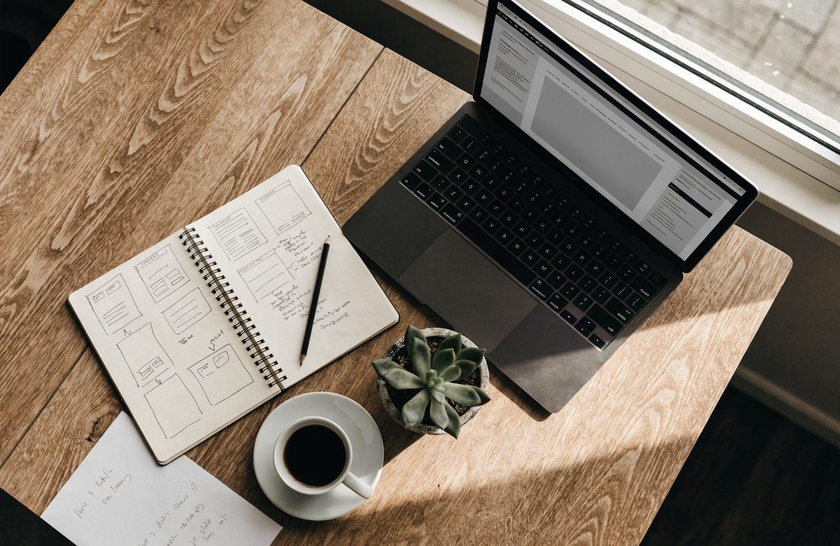A desk with a laptop showing a website layout and a notebook of page sketches